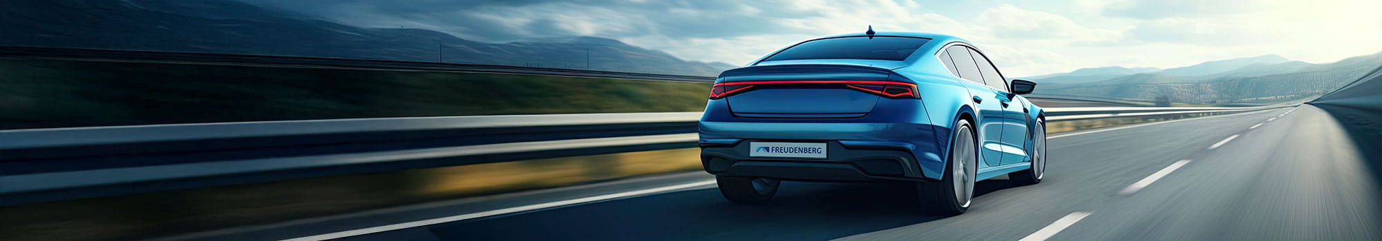 A blue car drives on an empty highway under a partly cloudy sky with mountains visible in the distance.